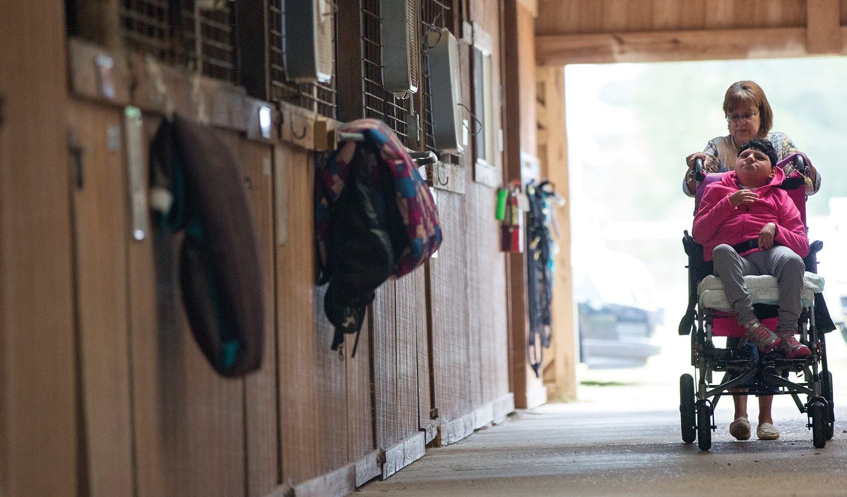 Maria Martinez wheels her daughter, Emelly, through SIRE Therapeutic Horsemanship’s stable in preparation for her horseback ride.