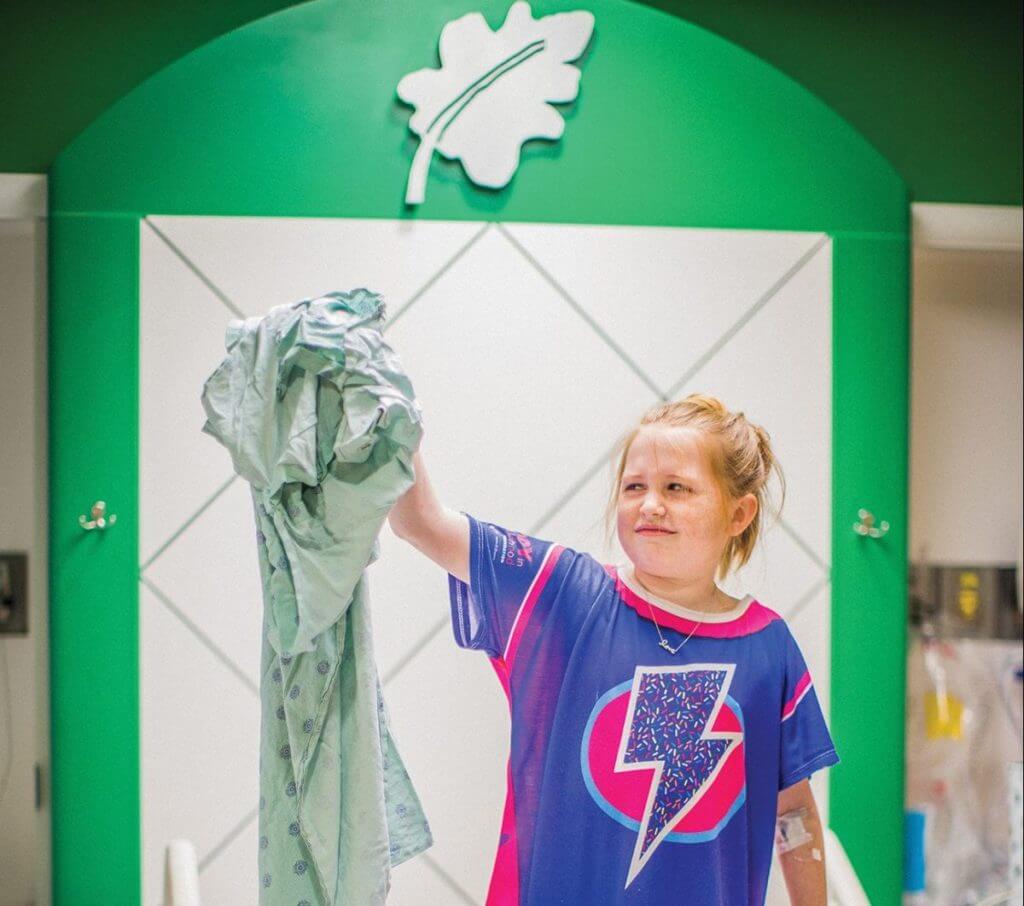 Evie Baxter, an 11-year-old patient at Children’s Memorial Hermann Hospital, sports her Starlight gown while holding an old, traditional gown for comparison.